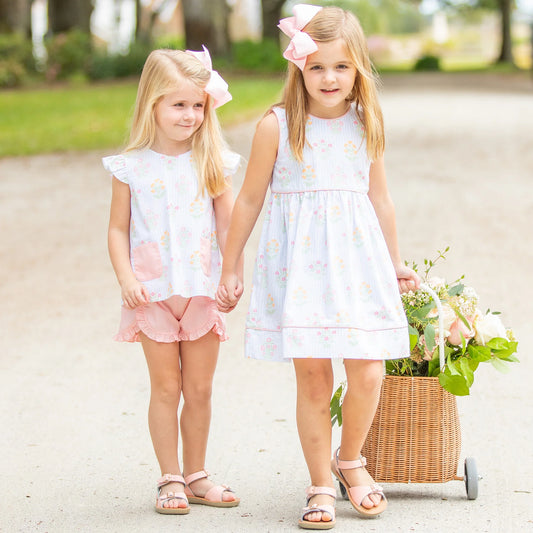 2 little girls dressed in Easter outfits pulling a basket of flowers behind them