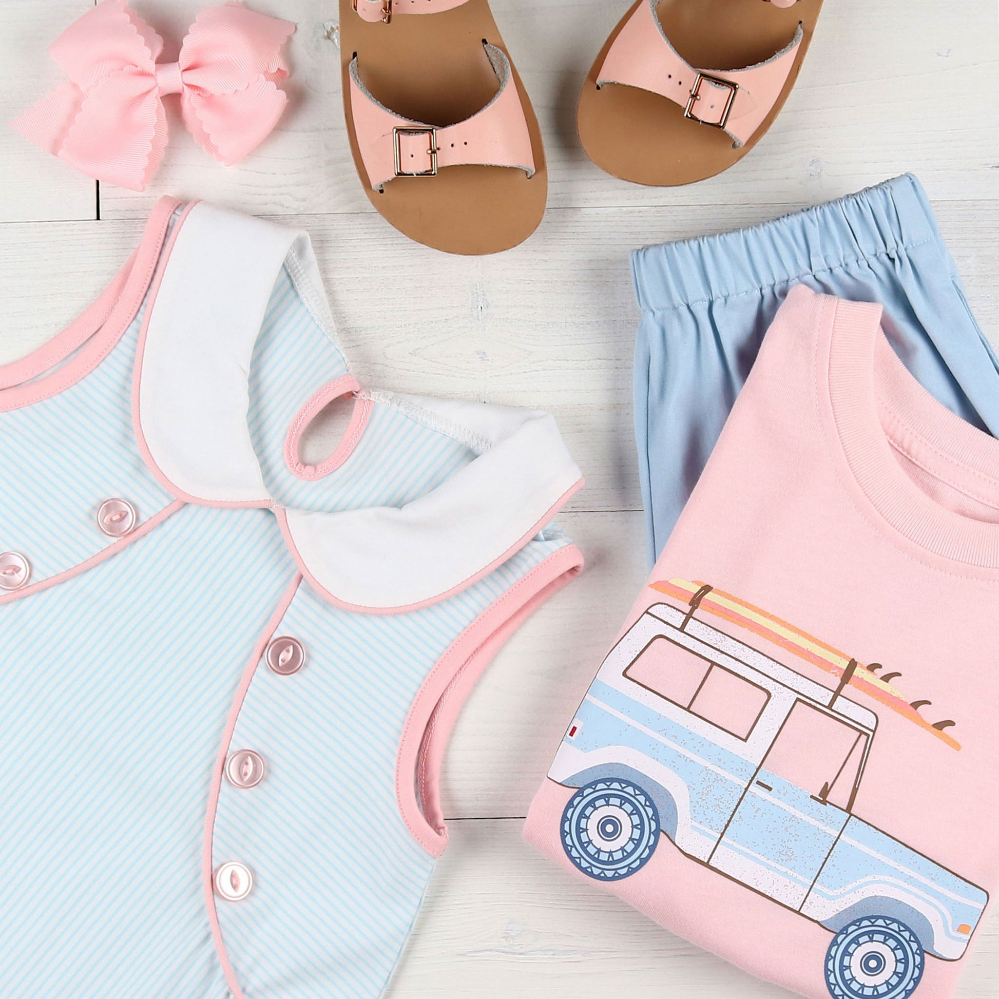 flatlay of Briggs Blue Knit Shorts, bronco graphic tee, aqua and white striped dress, pink sandals and a pink bow