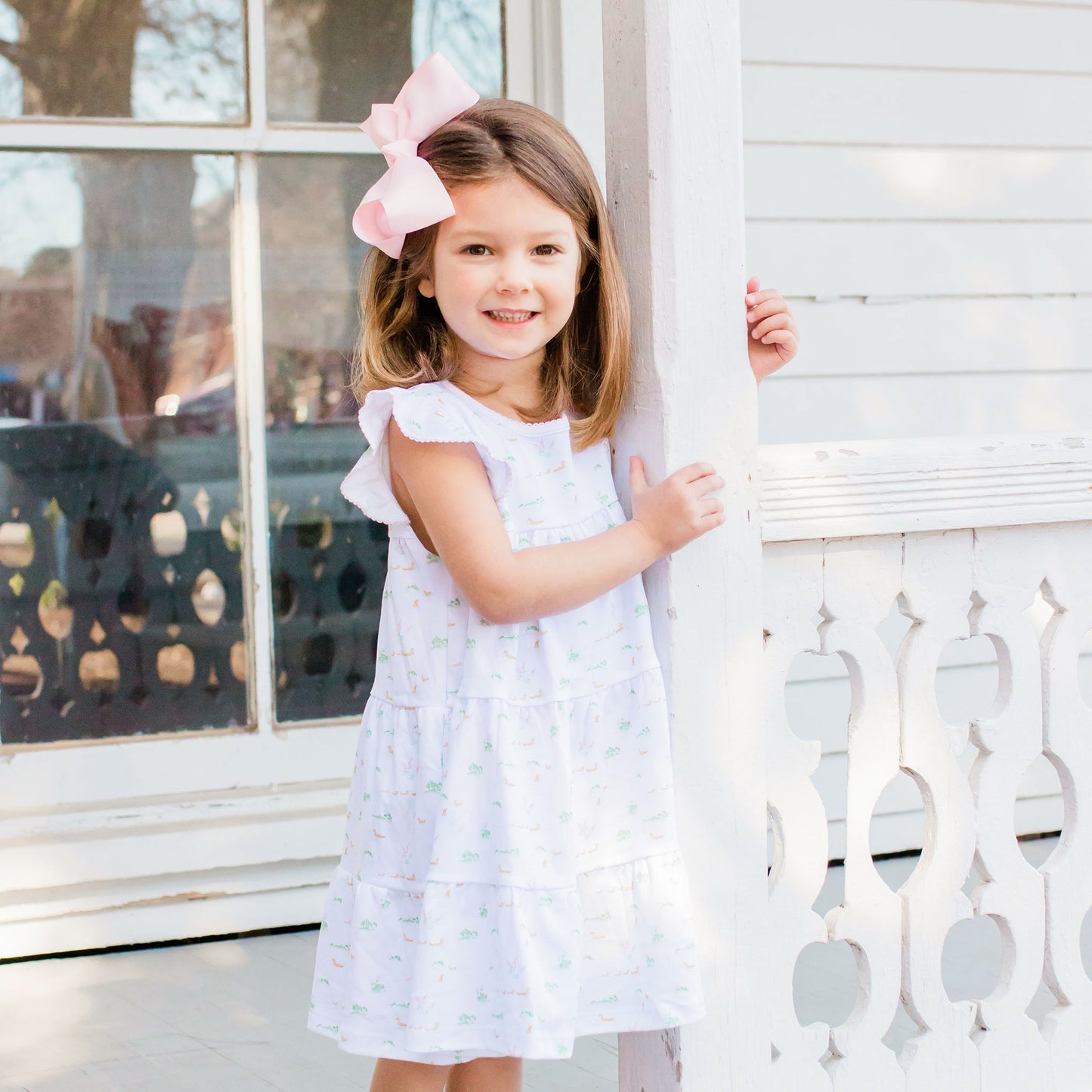 little girl with a pink bow standing on the porch of a house