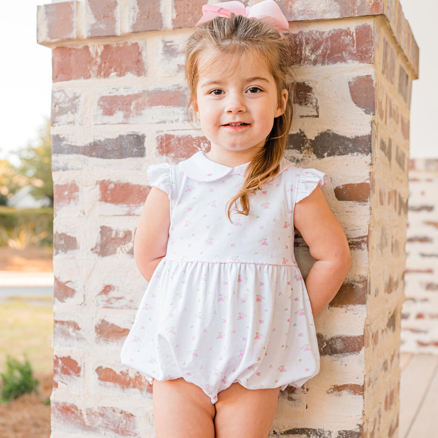little girl leaning against a cement column smiling