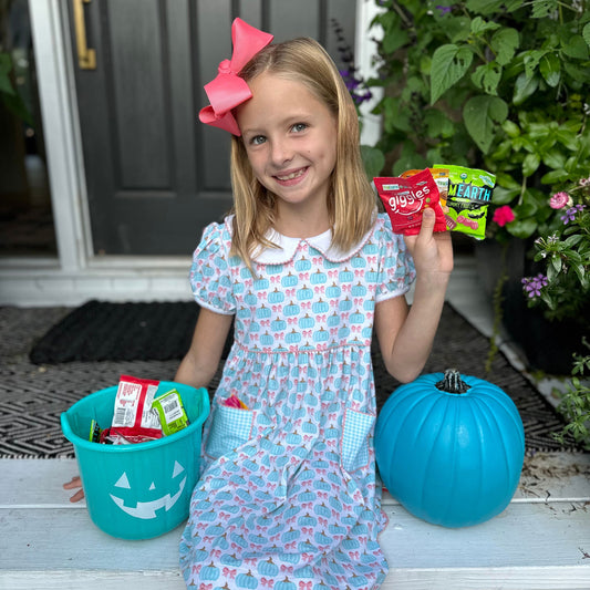 little girl on her front porch holding healthy snacks for halloween - the teal pumpkin project