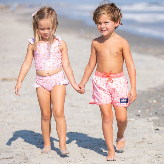 2 kids holding hands and walking down the beach
