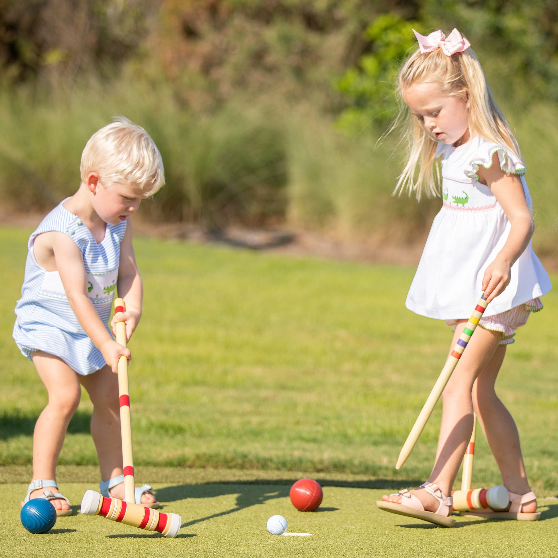 little girl wearing Kiawah Pink Smocked Alligator Set playing croquet with her brother