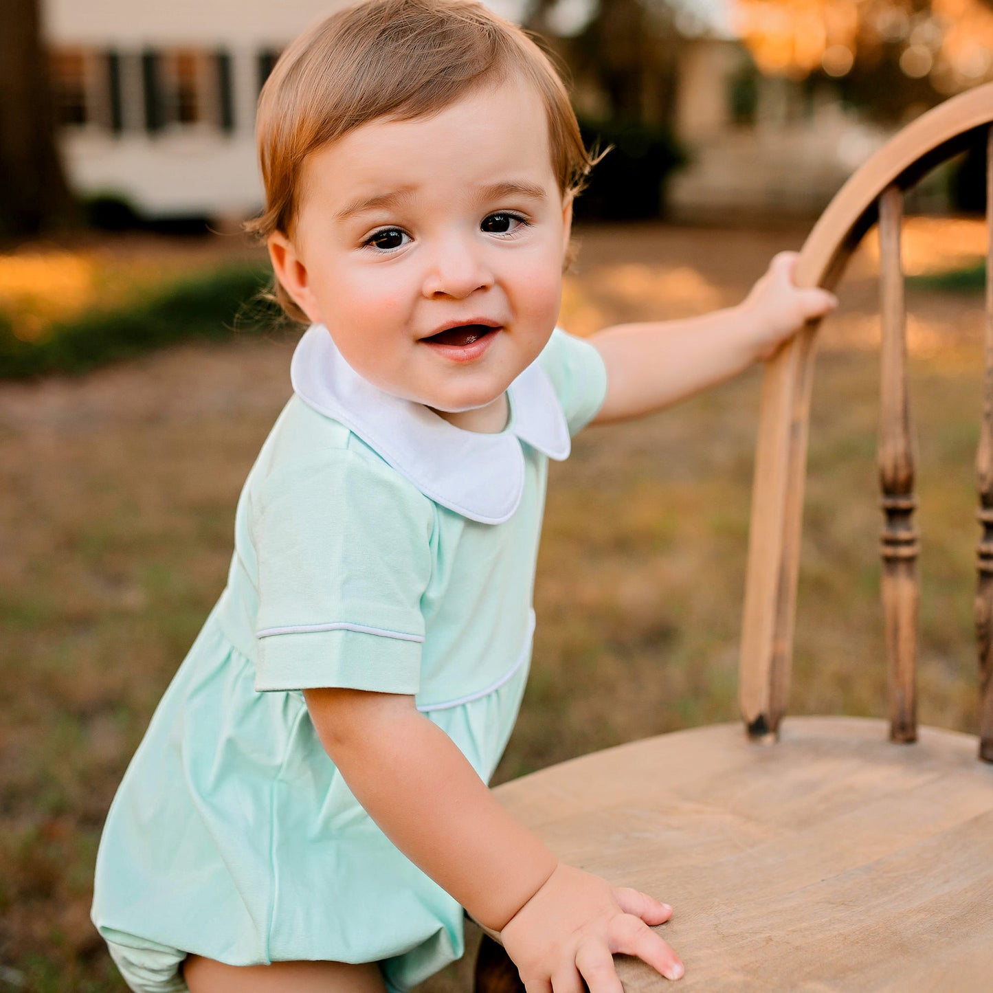 little boy holding on to a chair in the grass smiling