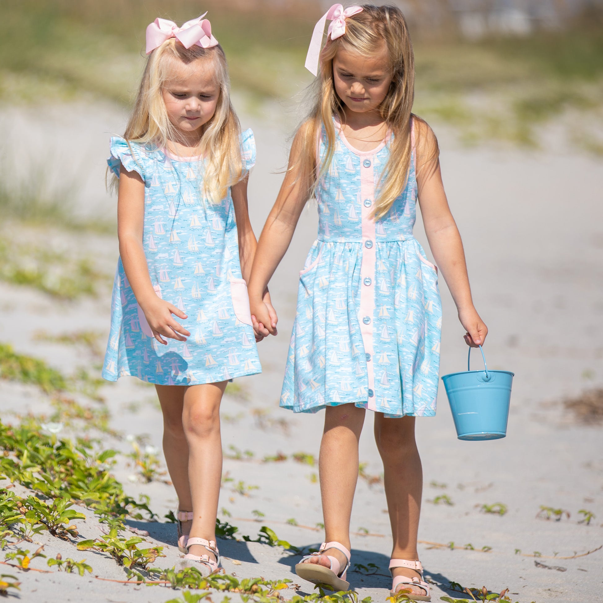 two little girls on the beach holding a beach bucket