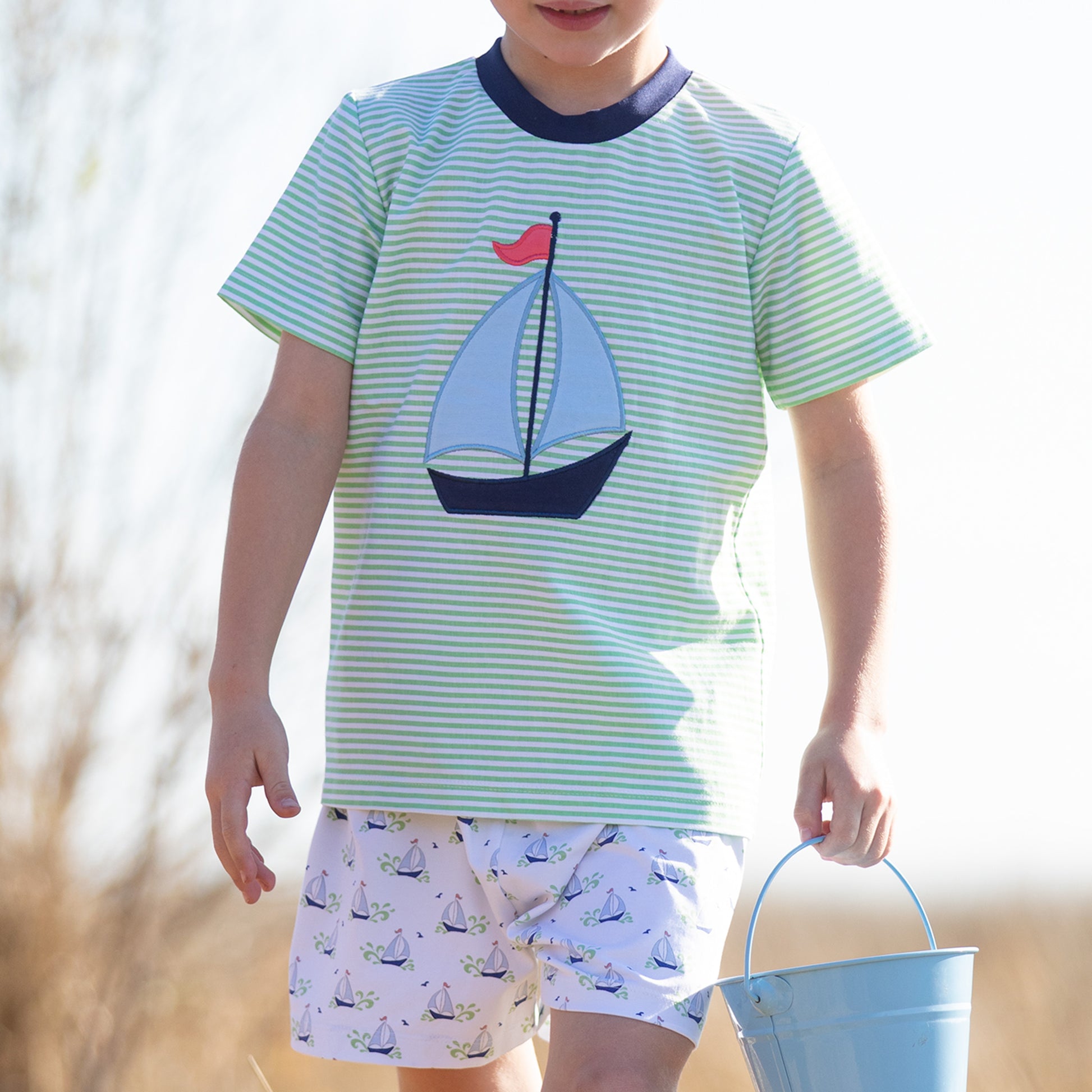 a boy wearing Beneteau T Shirt Set and holding a sand pale on the beach