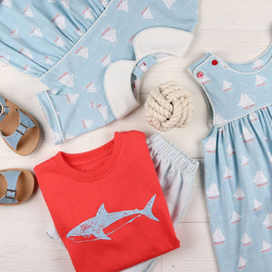 flatlay of sandals, shark shirt, shorts, sailboat jumper and shirt