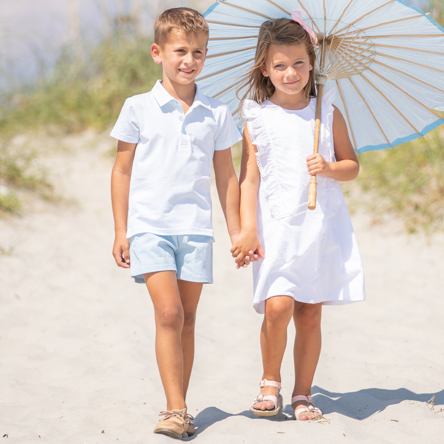 little girl and boy holding hands walking down the beach with a parasol