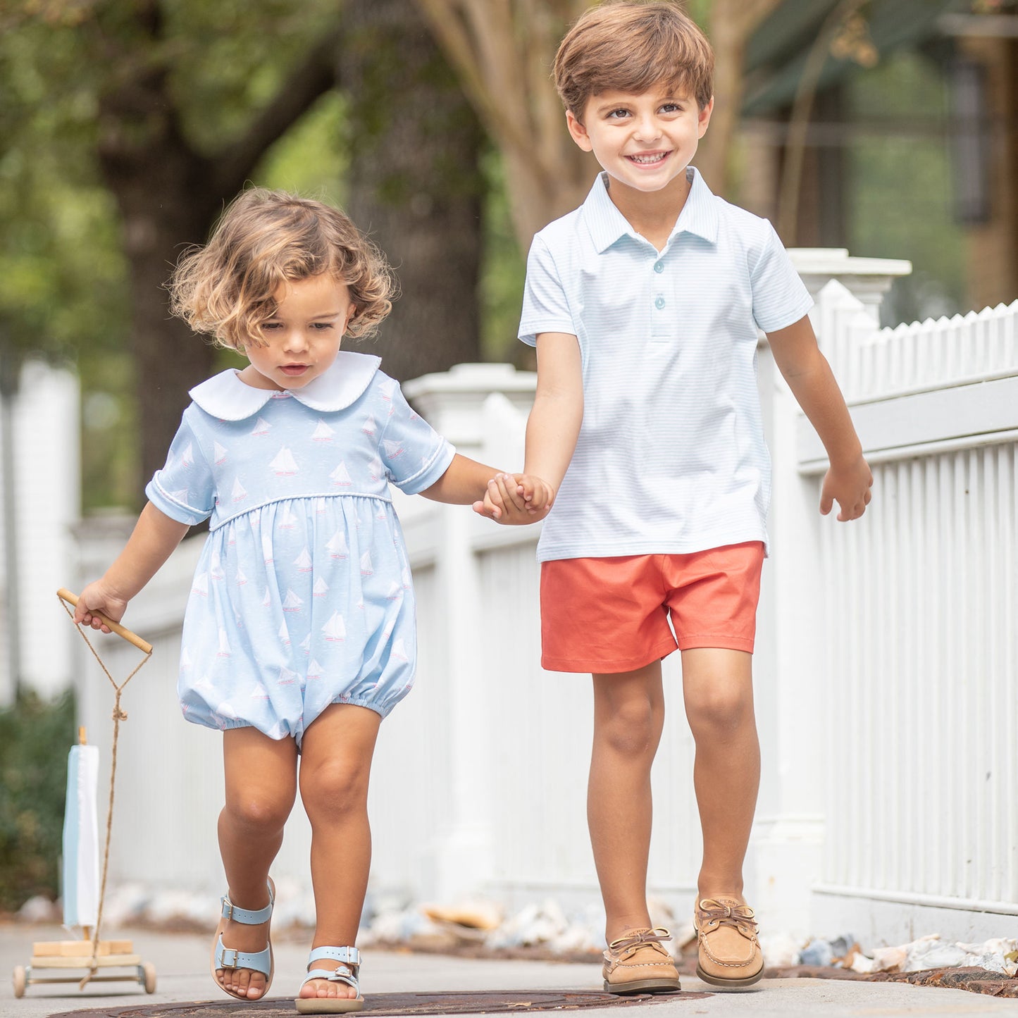 little boy wearing a Tennis Club Stripe Polo holding his little brother's hand walking down the sidewalk in a neighborhood