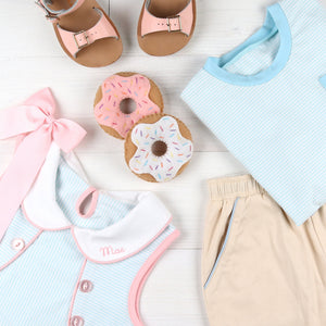 flatlay of shorts, tshirt, dress, bow, sandals and play donuts