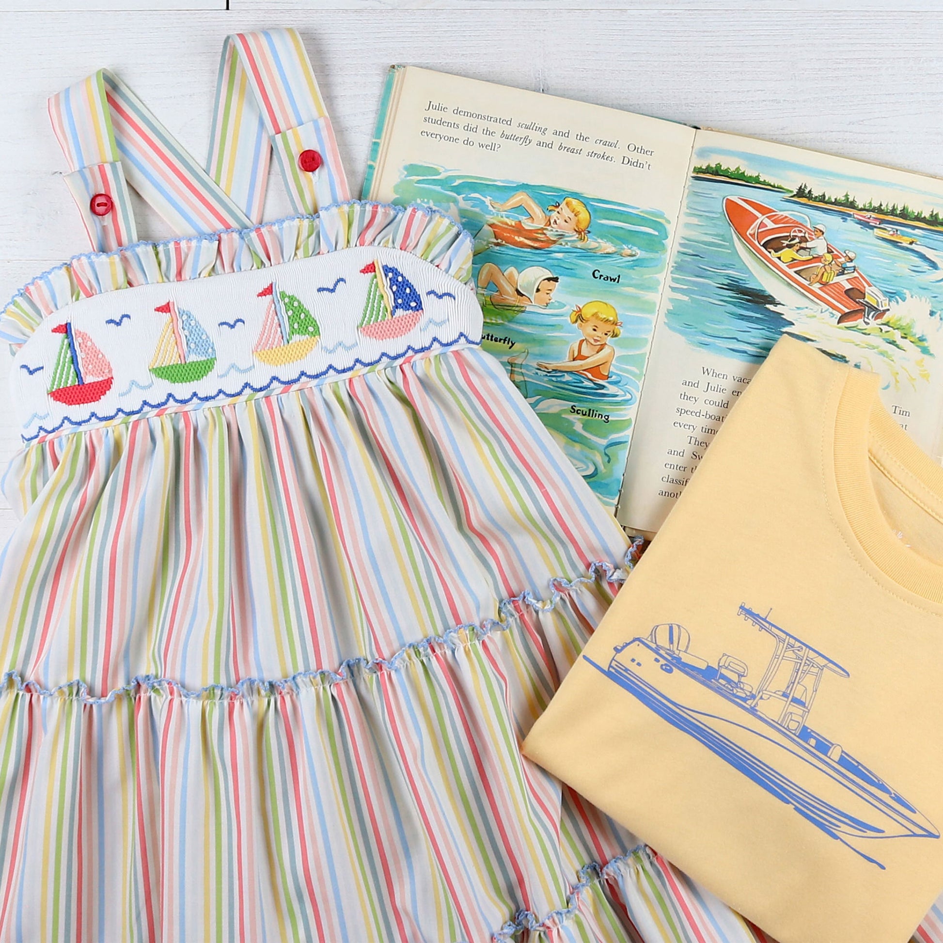 flatlay of sailboat dress, tshirt and a book