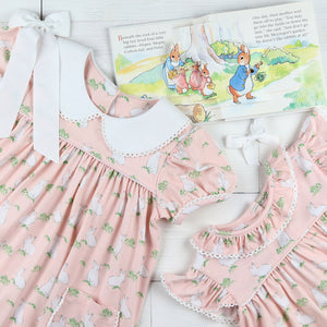 flat lay of 2 dresses with a bunny book and white bow