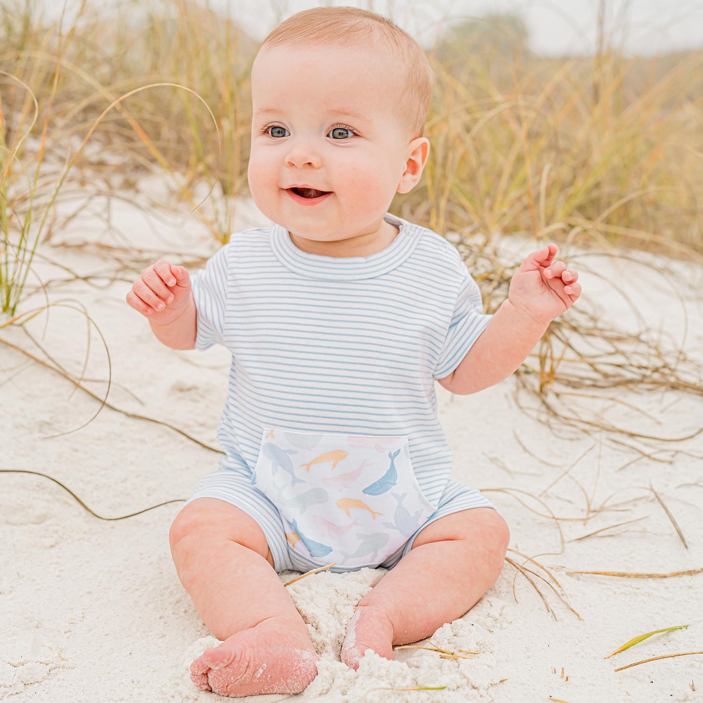 little baby sitting in the sand wearing a Colorful Whale Pima Romper