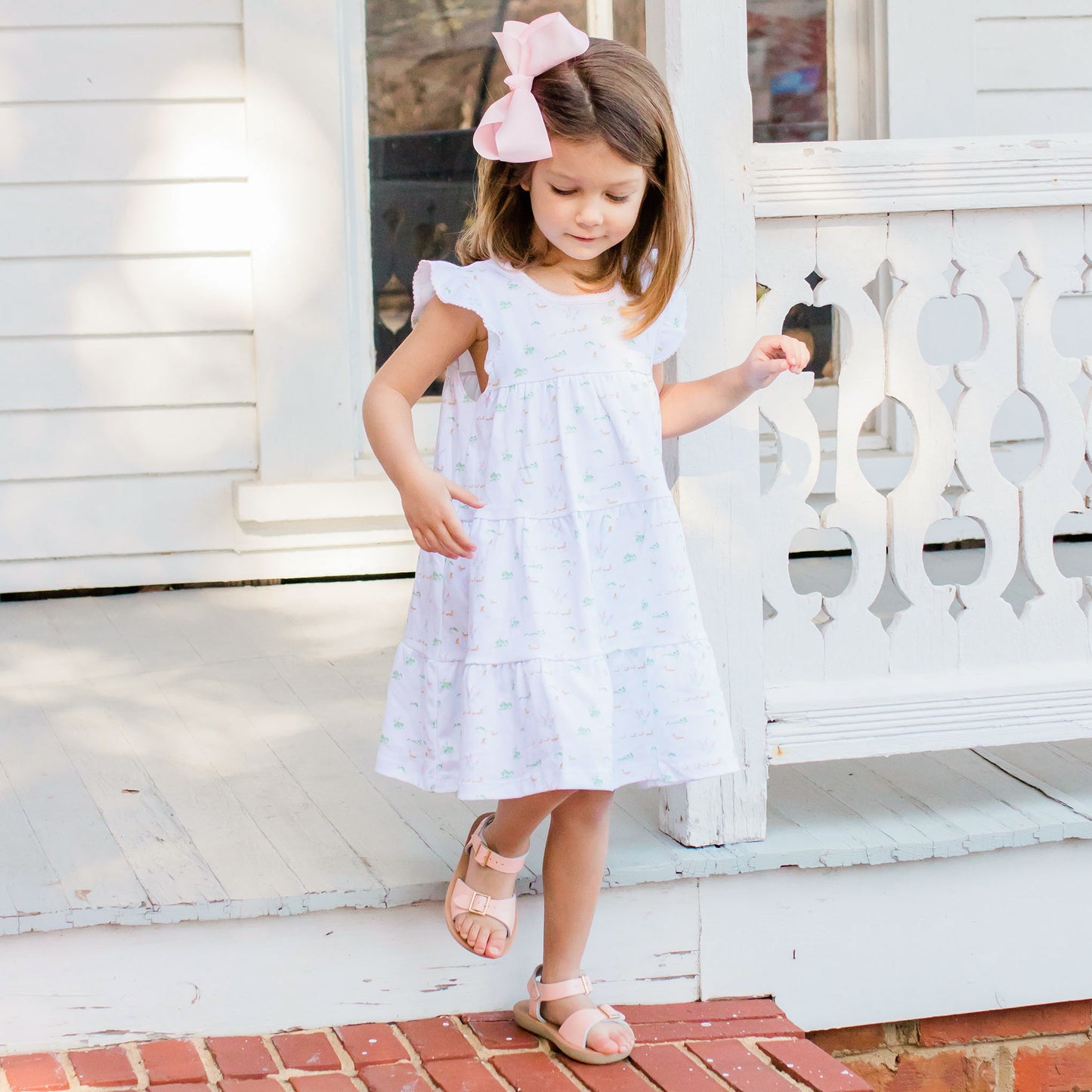 little girl wearing a Ducky Pima Flowy Dress, with a pink bow in her hair and pink sandals walking down the porch steps