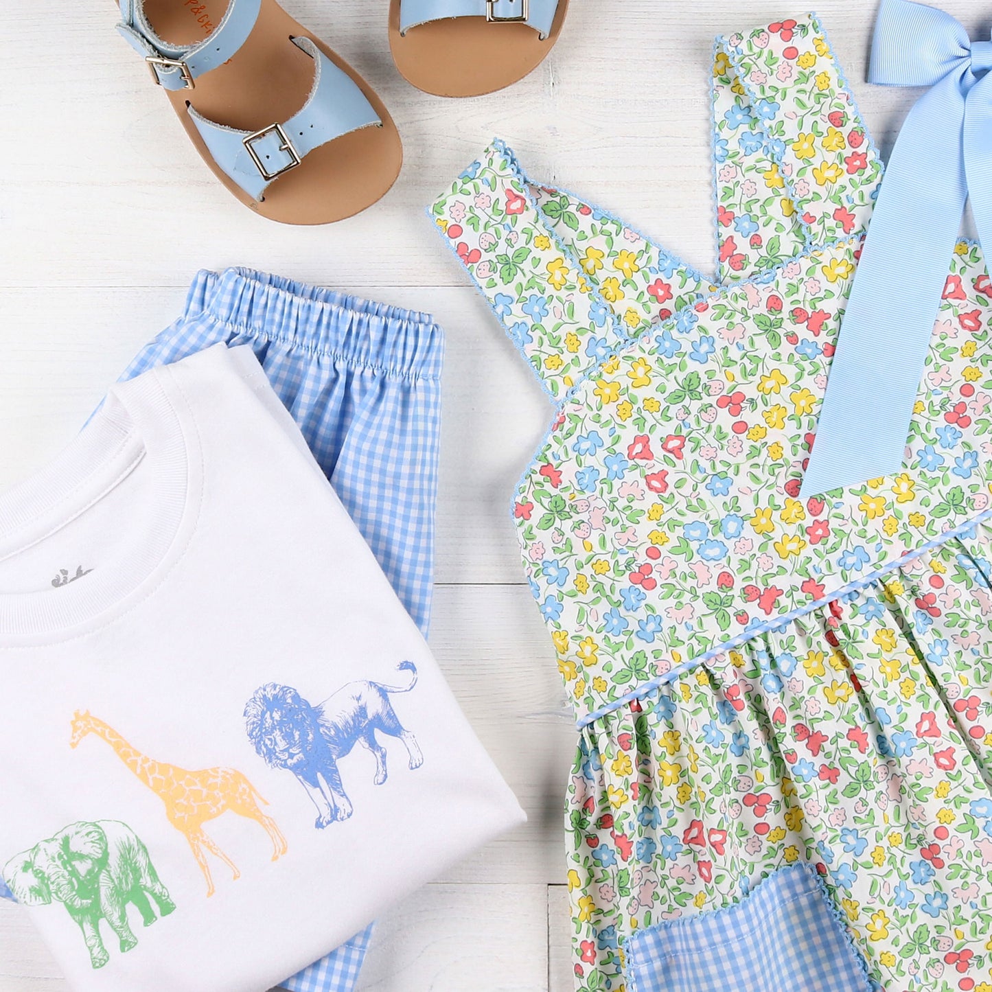 flatlay of tshirt with safari animals, dress, light blue bow and sandals and shorts