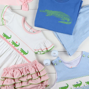 flat lay of graphic tee, pink bow, alligator shirt, ruffle bloomers