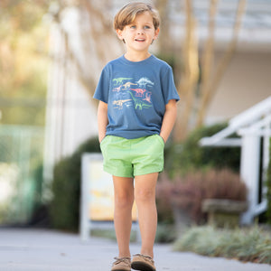 little boy smiling on the sidewalk wearing a Dinosaur Graphic Tee and green shorts
