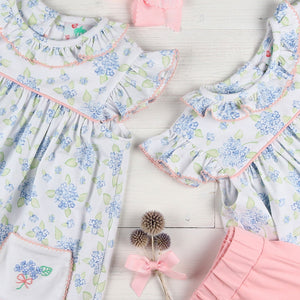 flatlay of 2 dresses, pink shorts and a pink bow