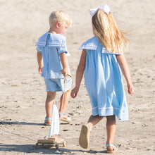 Load image into Gallery viewer, little boy wearing Boys Sail Away Set pulling a wooden toy sailboat with his sister at the beach