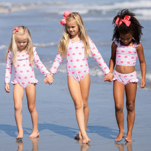three little girls holding hands walking down the beach