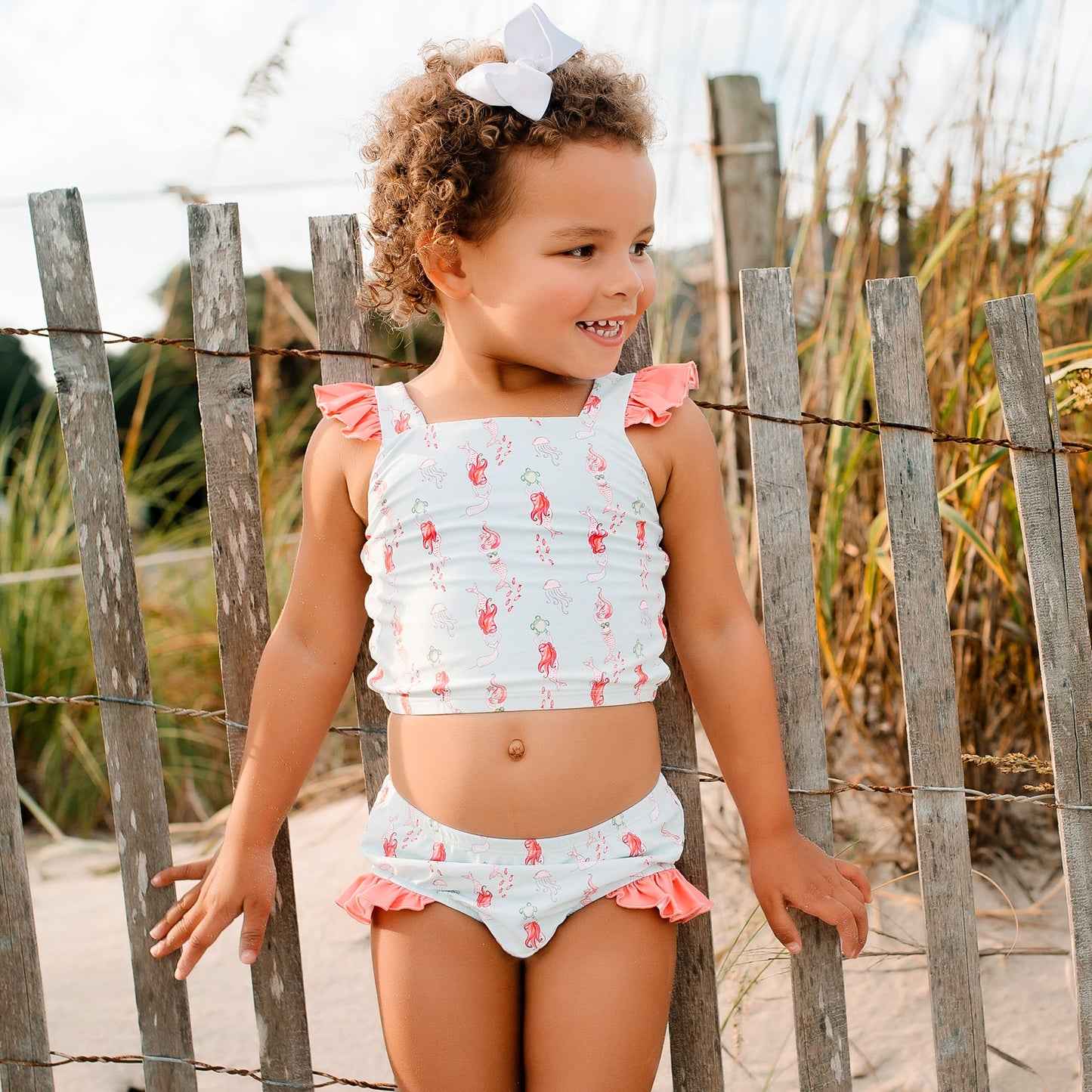 little girl at the beach smiling by a fence post