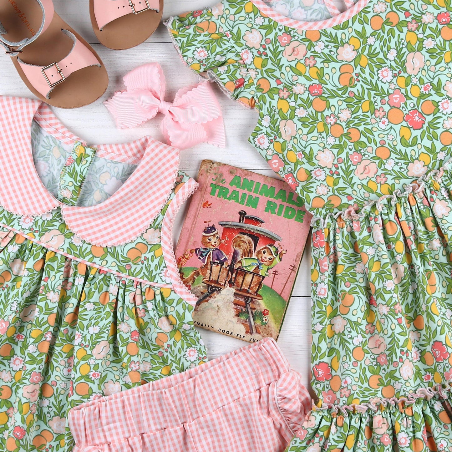flatlay of Girls Orange Blossom Swing Top, dress, shorts, books, bow and sandals
