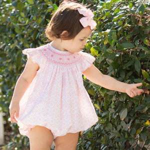 little girl wearing Petit Rose Smocked Bubble and touching a bush