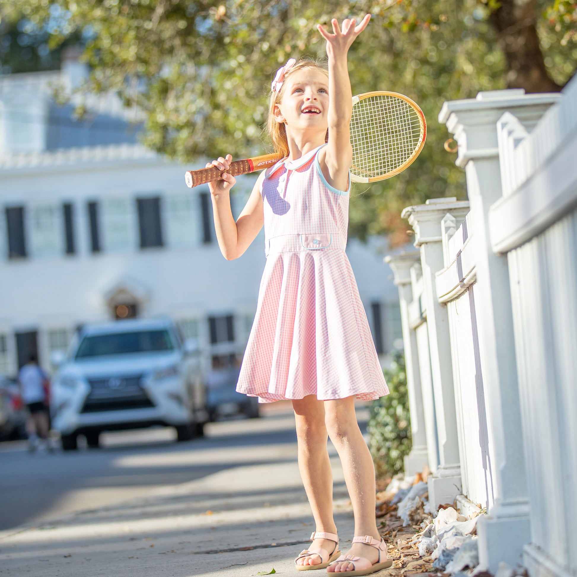 little girl holding a tennis racket on the sidewalk