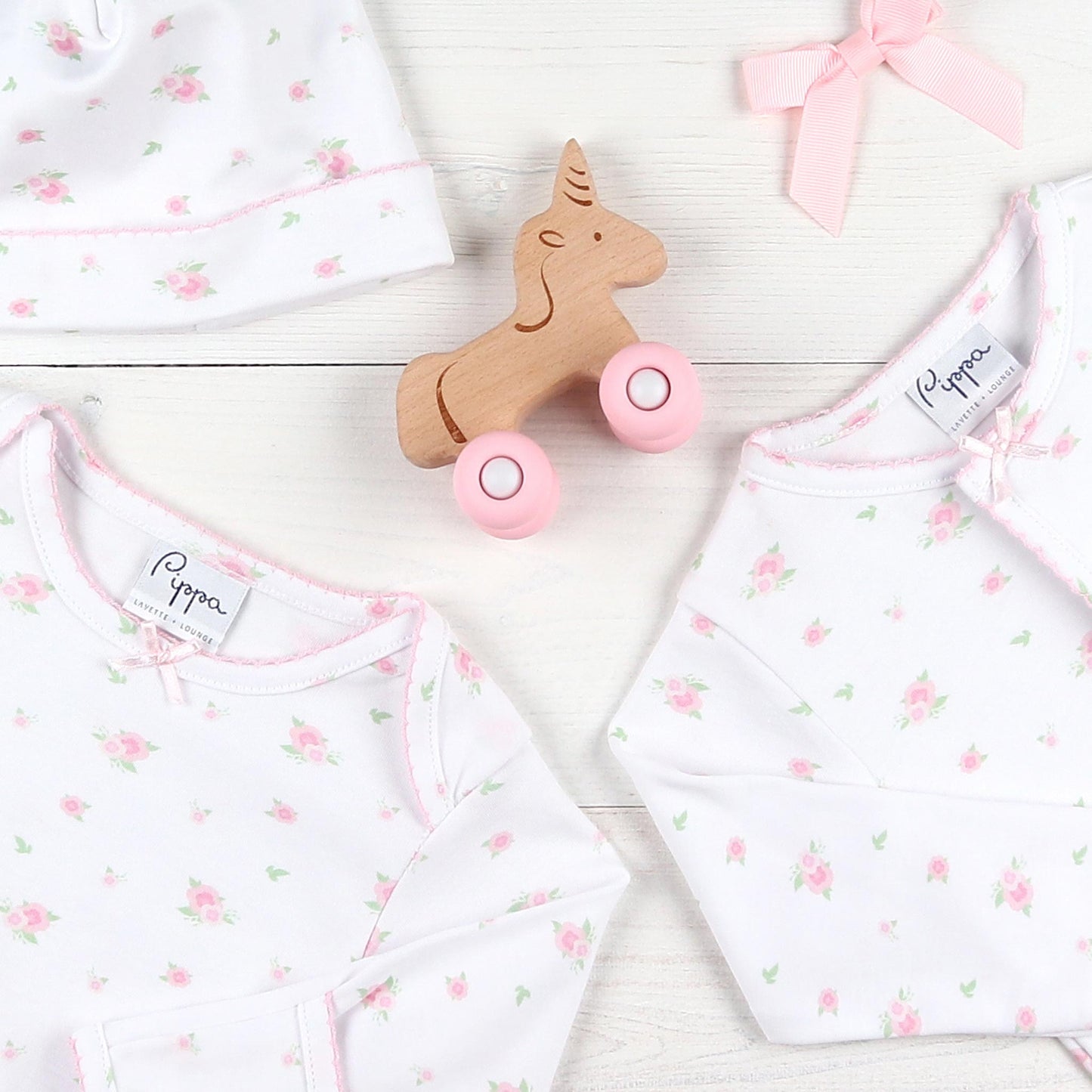 flatlay of flowered pajamas, pink bow and a wooden toy unicorn