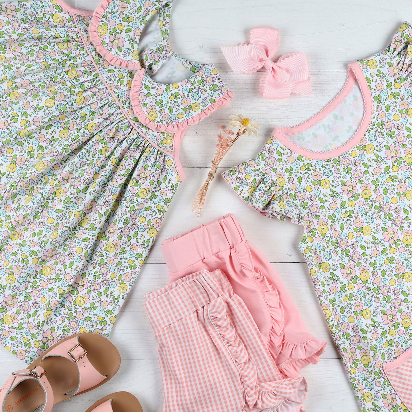 flatlay of flowered dress, pink sandals, pink bow and pink shorts