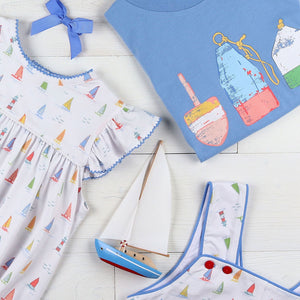 flatlay of Buoy Graphic Tee Shirt, saliboat dress, sailboat toy, light blue bow and a jon jon