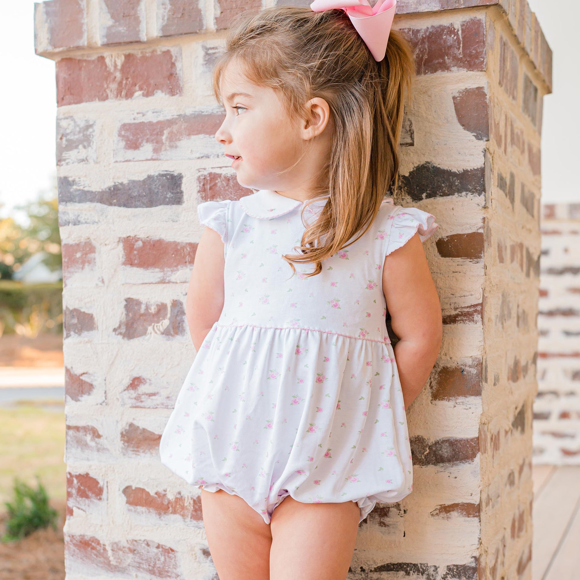 little girl leaning against a pole wearing Girls Rosette Pima Bubble with a pink bow in her hair
