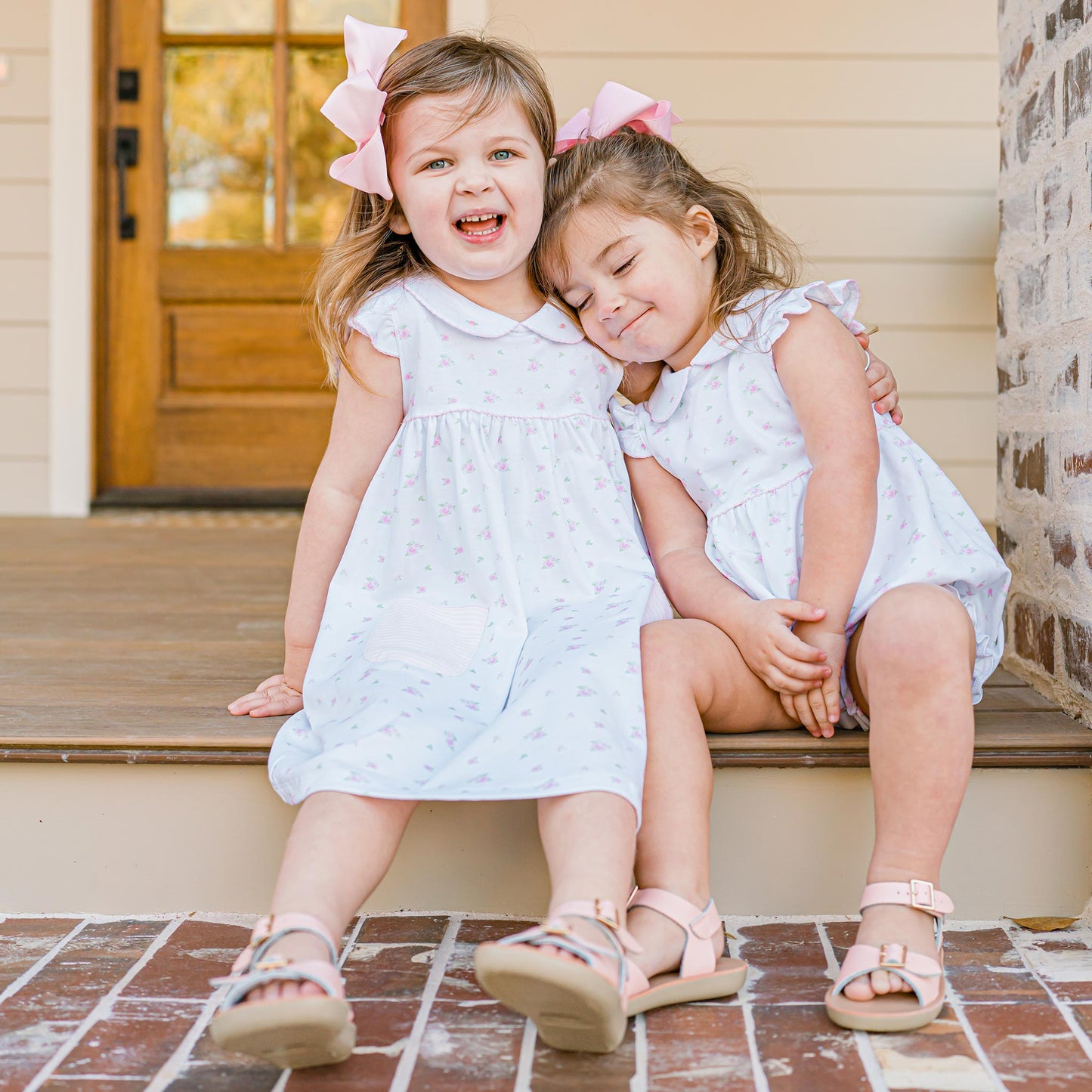 two little girls sitting on the porch with one little girl wrapping her arm around another girl