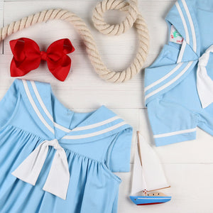 flatlay of Light Blue Sail Away Dress, red bow, rope, toy sailboat and blue jon jon