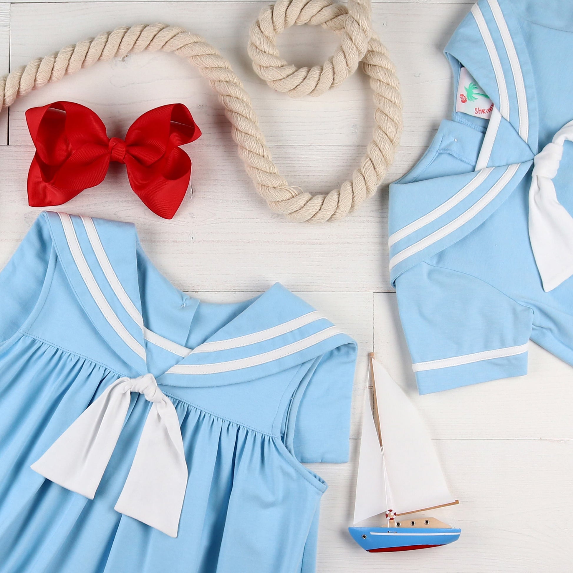 flatlay of Light Blue Sail Away Bubble, toy sailboat, red bow, rope and boys jumper