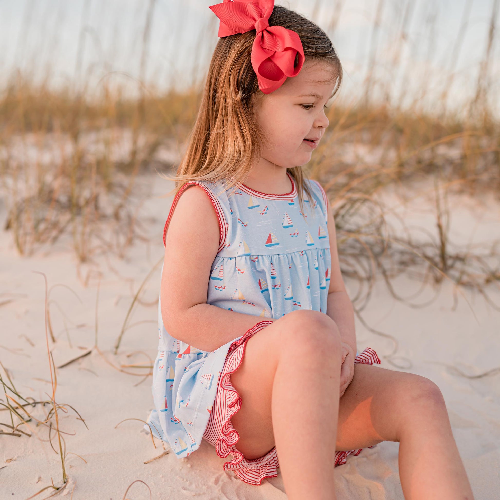 little girl sitting at the beach with a big red bow in her hair