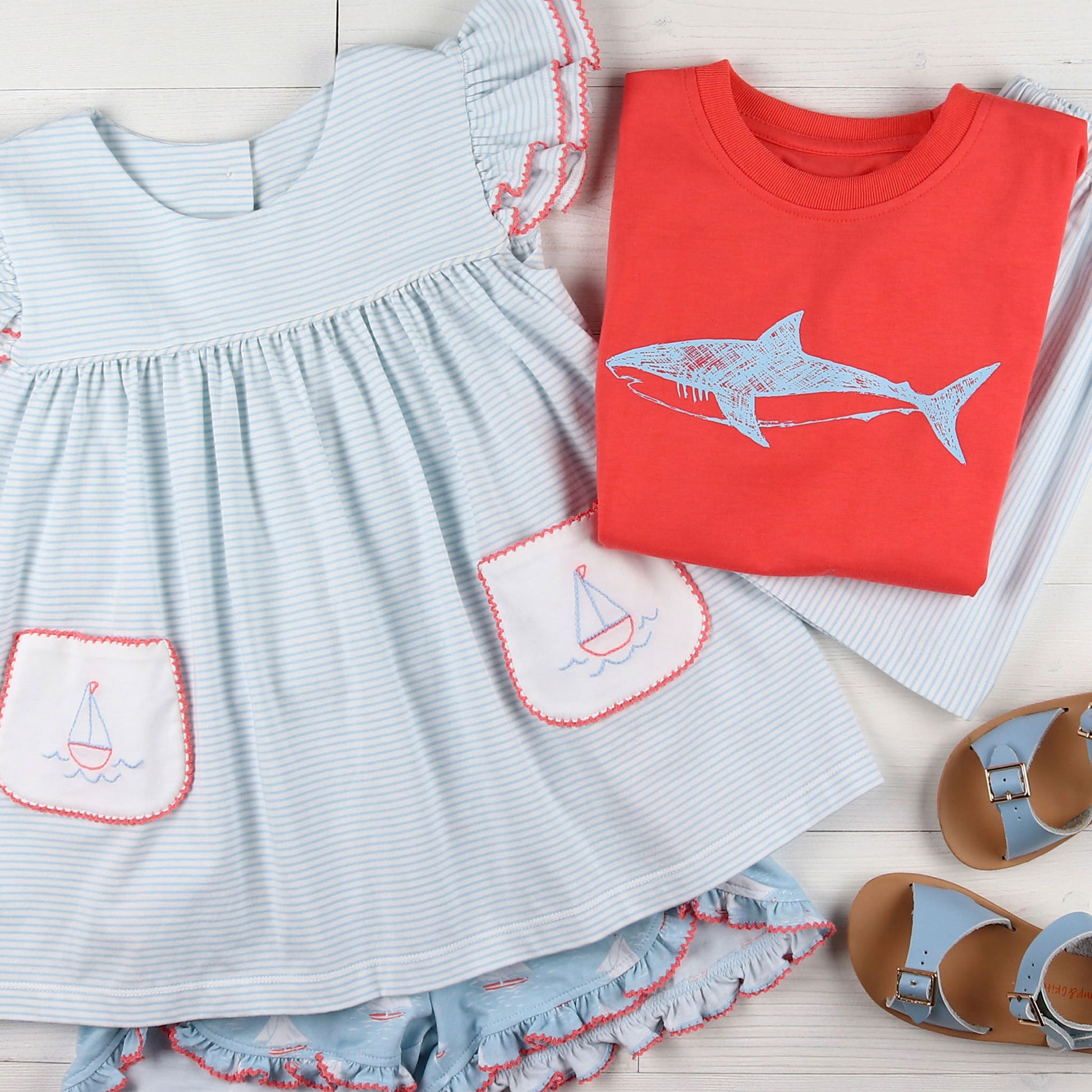 flatlay of striped girls outfit, light blue sandals, red shark graphic tee