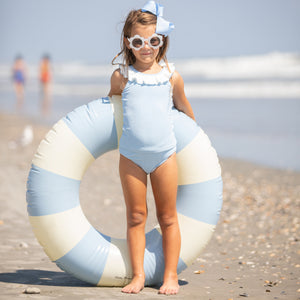 little girl holding blue and white striped floatey in her sunglasses and bow at the beach