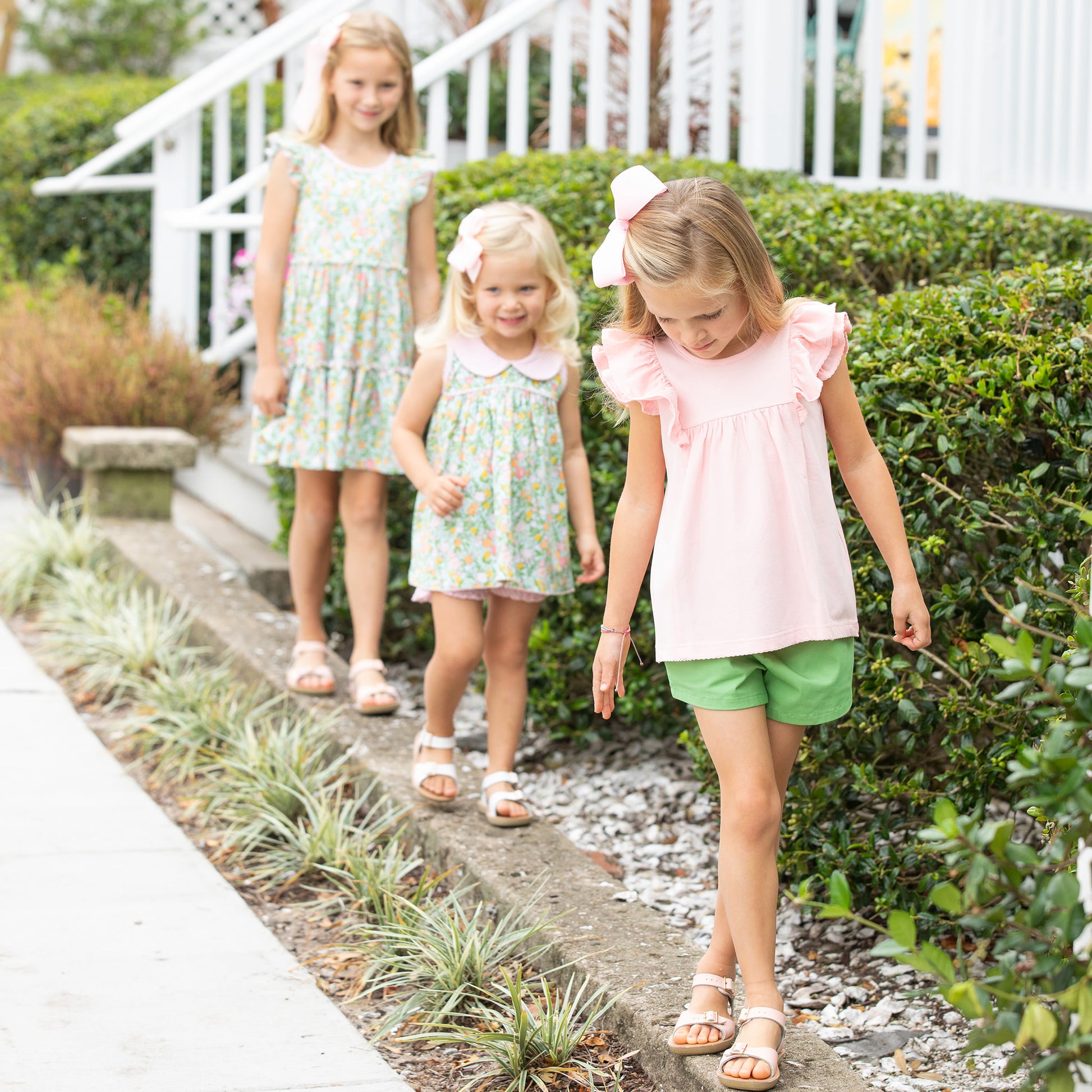 three little girls walking on the edge of the sidewalk smiling