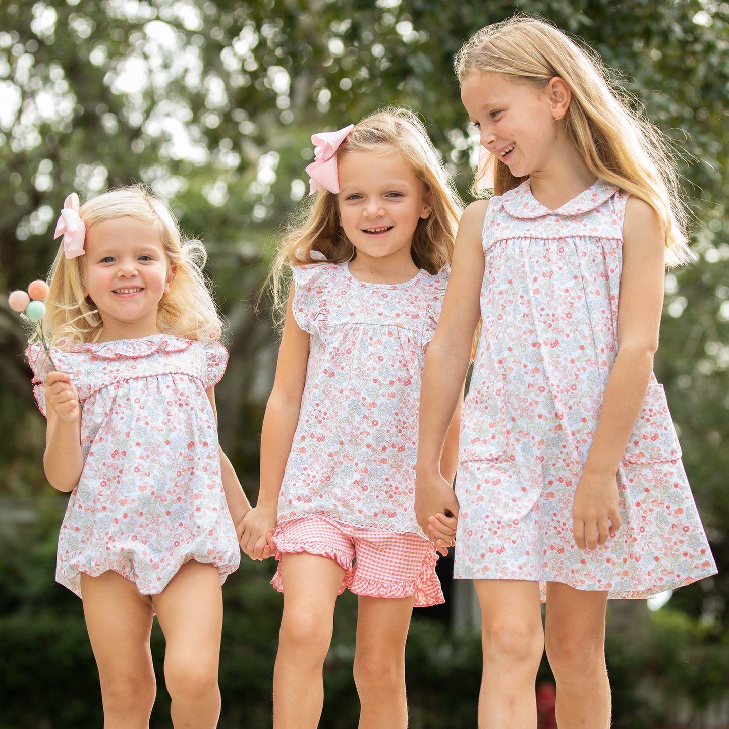 Three little girls holding hands and walking in slowered shirts and dresses