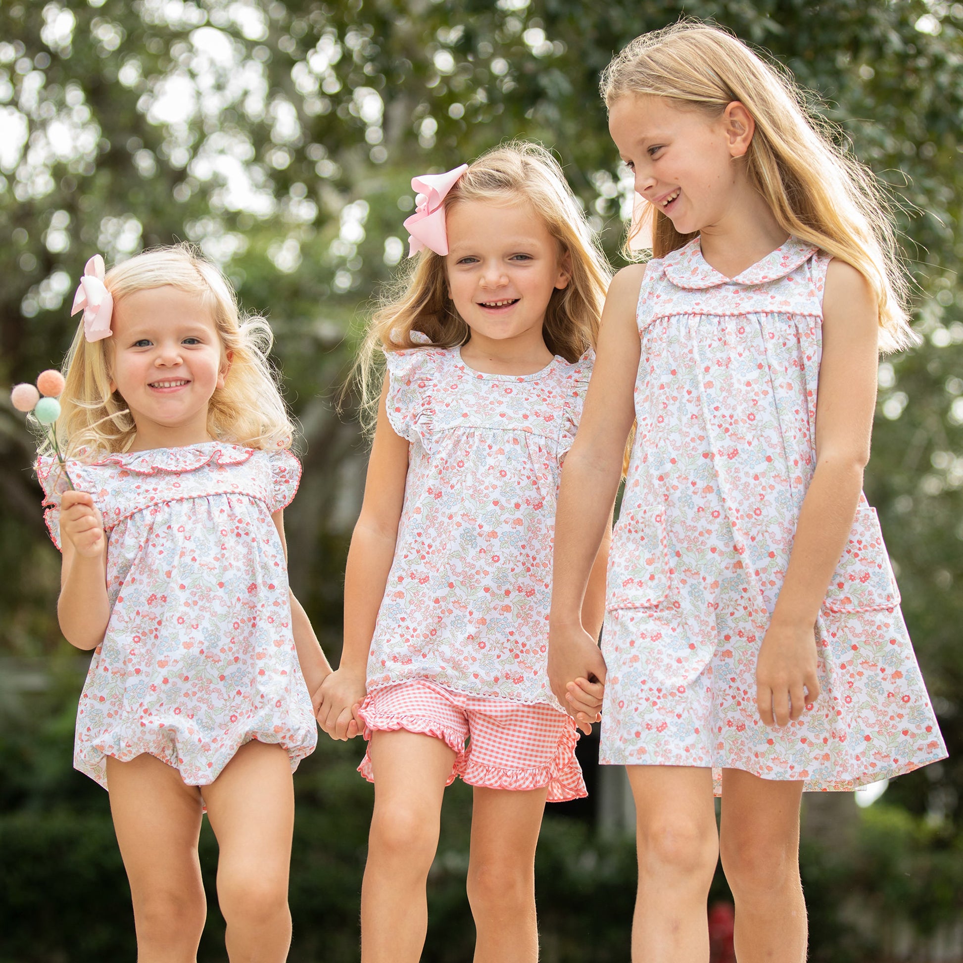 Three little girls holding hands and walking in slowered shirts and dresses
