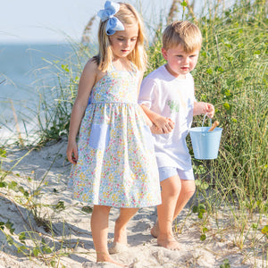 little girl in Sunny Floral Bow Back Dress and brother holding hands on the beach