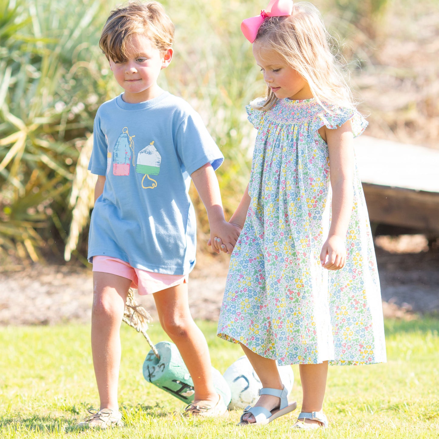 little boy and little girl wearing Sunny Floral Smocked Bishop holding hands walking through the grass