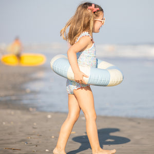 little girl playing at the beach in blue striped floaty