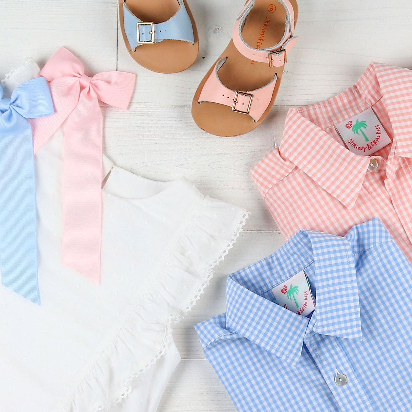 flatlay of a white dress, blue and pink hair bow, sandals and boys oxford shirts