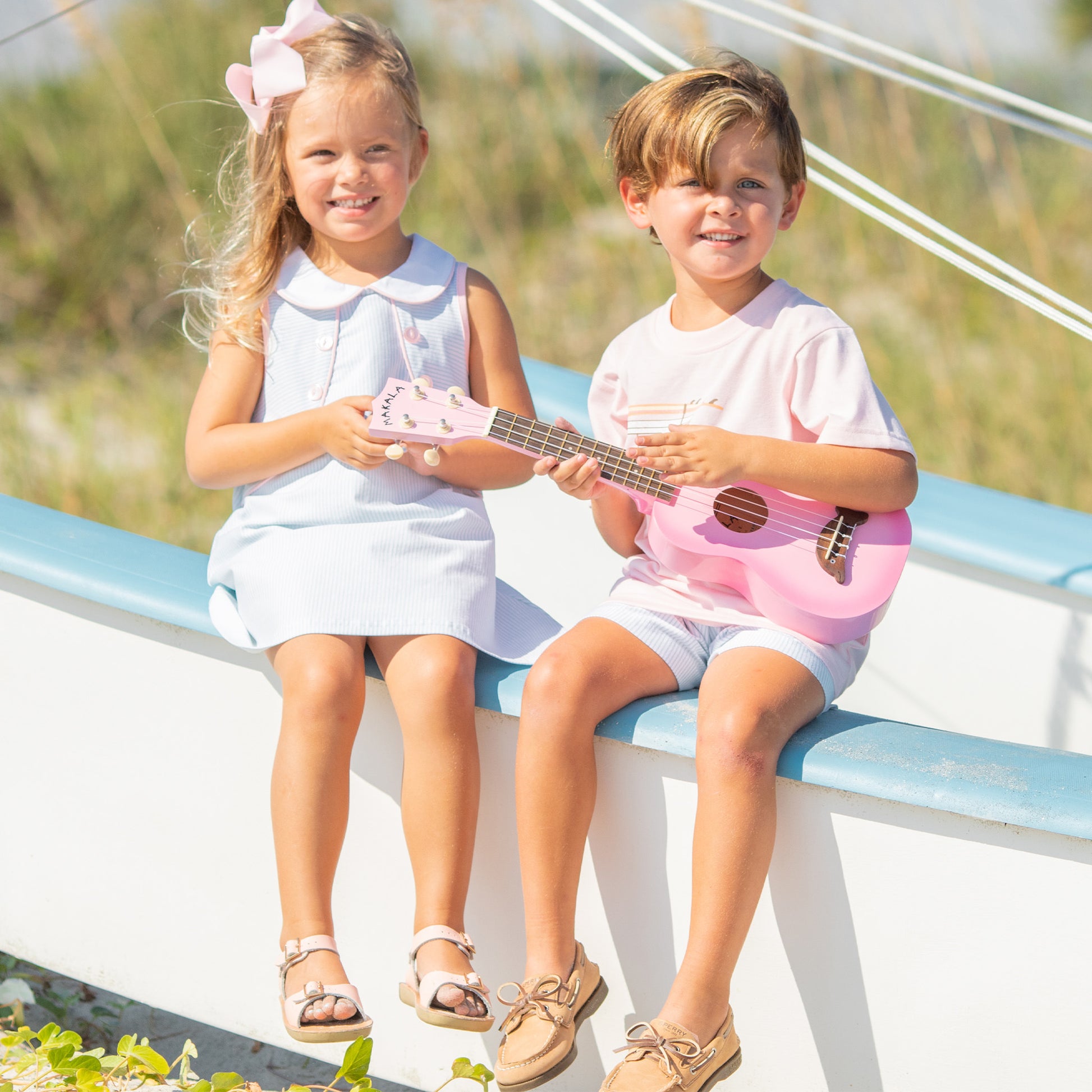 little boy holding a pink play guitar sitting on the boat with a little girl