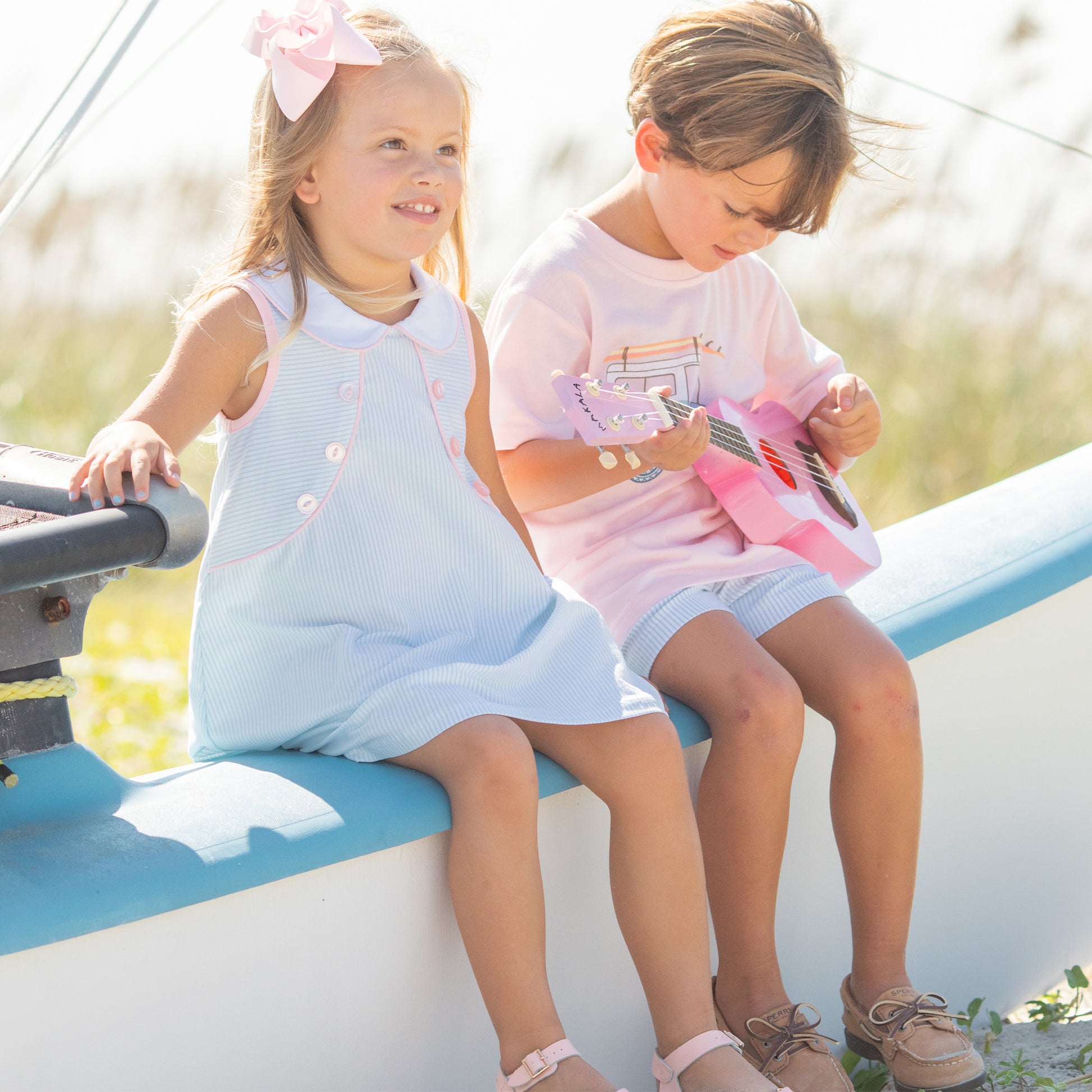 little girl wearing a Girls Tennis Club Eloise Dress sitting by a little boy on a boat at the beach